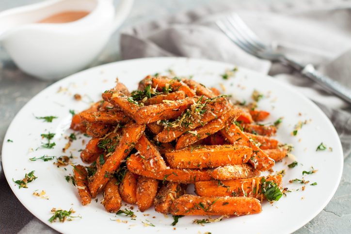 Baby carrots roasted with parmesan and herbs served with sauce on grey table