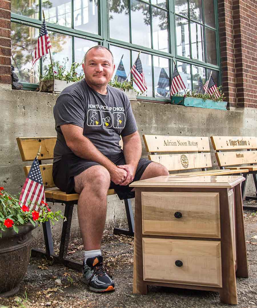 U.S. Army veteran Chad Diffin sits outside of the woodshop next to his most recent project, a two-toned nightstand.
