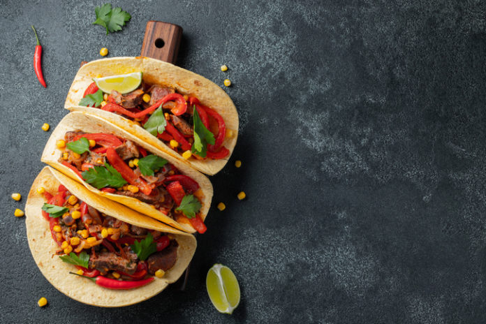 Mexican tacos with beef, vegetables and salsa. Tacos al pastor on wooden board on black background. Top view with copy space